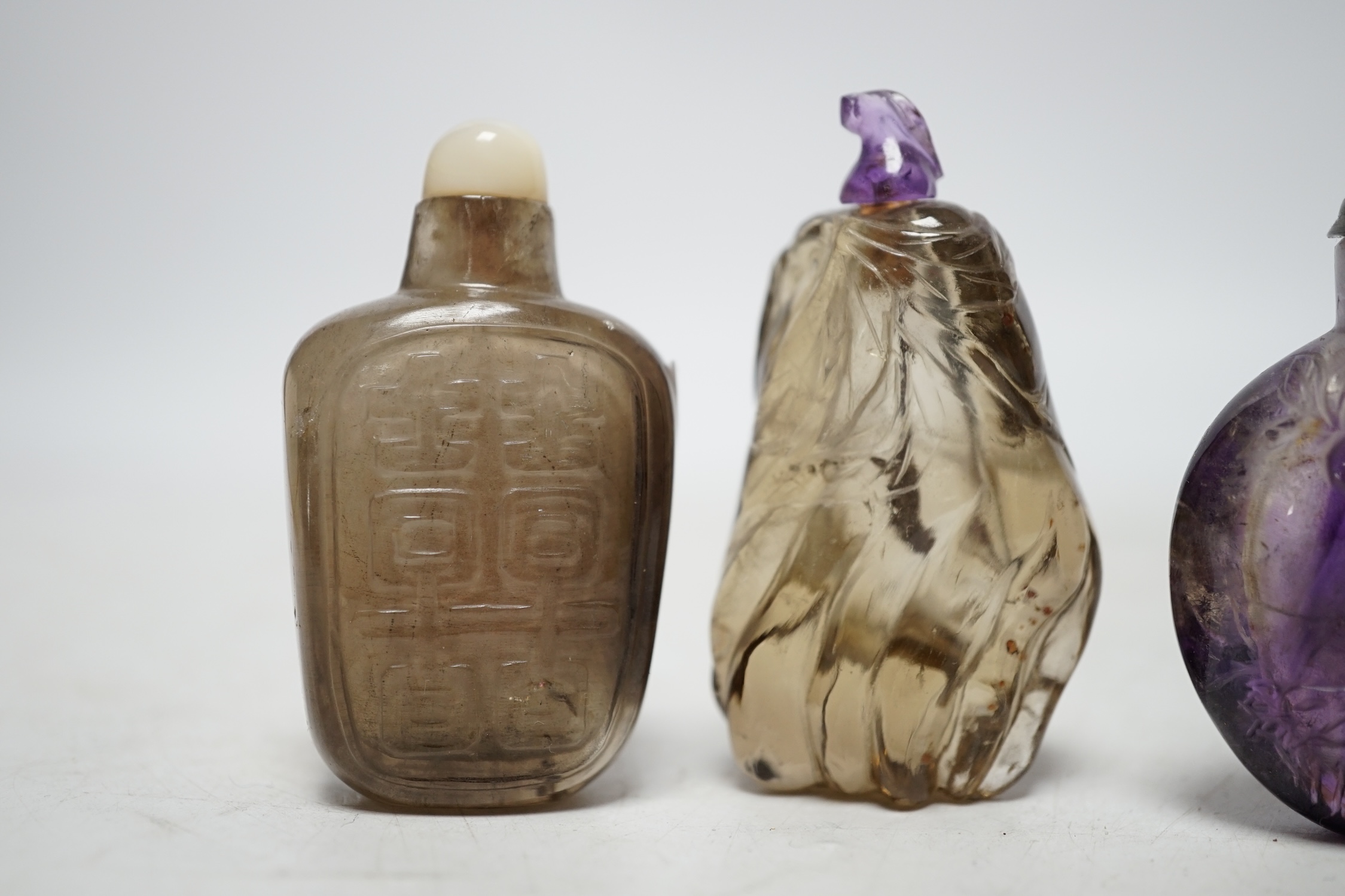 Three Chinese carved quartz snuff bottles, 19th/20th century to include a smoky quartz shuangxi bottle, an amethyst quartz bottle and a small smoky quartz gourd shaped bottle, largest 6.5cm high